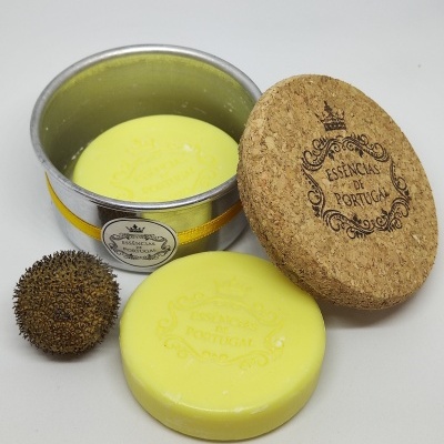 Sabonete amarelo redondo com embalagem metálica e tampa de cortiça, com esfera marrom texturada