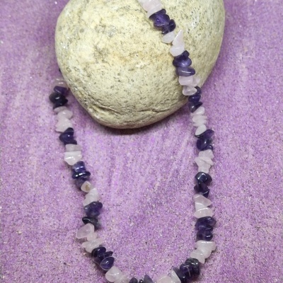 Colar de pedras naturais rosa e roxas sobre areia e pedra cinzenta