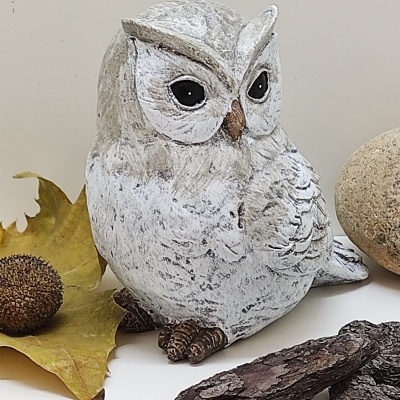 Figura decorativa de coruja branca e cinzenta com olhos negros e elementos naturais ao redor