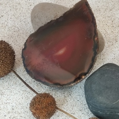 Ágata polida castanha e preta sobre pedras cinzentas com sementes secas marrons num fundo claro.