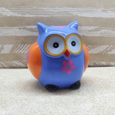 Figura de coruja azul e laranja com flores cor-de-rosa sobre superfície clara