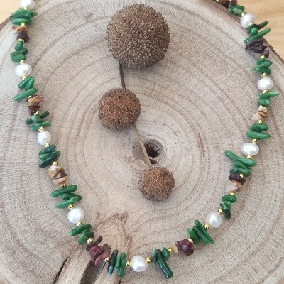 Colar com pedras verdes, pérolas e elementos castanhos sobre tábua de madeira com flores secas