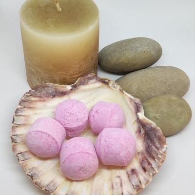 Vela bege, pedras cinzentas, concha com bombas de banho rosas