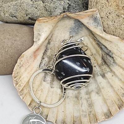 Chaveiro com esfera preta e pendente metálico sobre concha e pedras