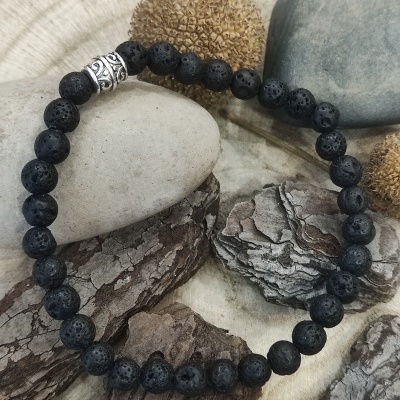 Pulseira de contas negras de lava vulcânica com detalhe metálico prateado sobre pedras e casca seca