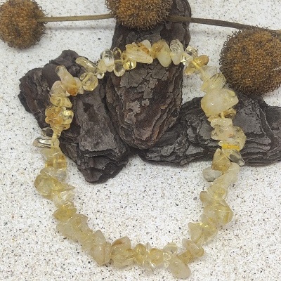 Pulseira de pedras de citrino amarelo sobre fundo claro com madeira escura e bolas secas de plantas