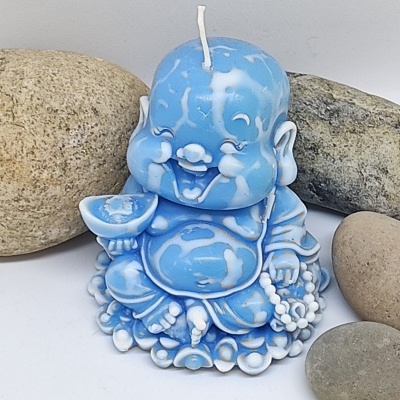 Vela azul e branca em forma de Buda sorridente rodeada por pedras cinzentas.
