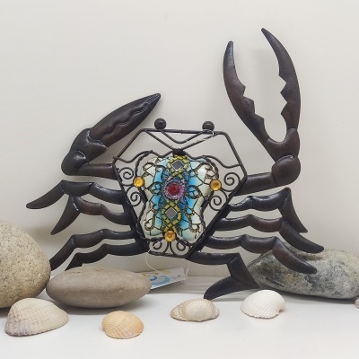 Escultura decorativa de caranguejo em metal com vidro colorido rodeada por conchas e pedras
