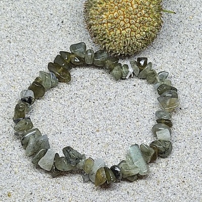 Pulseira verde de pedras irregulares sobre areia ao lado de fruto seco espigado verde