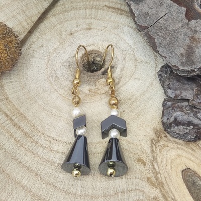 Brincos com contas douradas, pérolas e elementos pretos em fundo de madeira