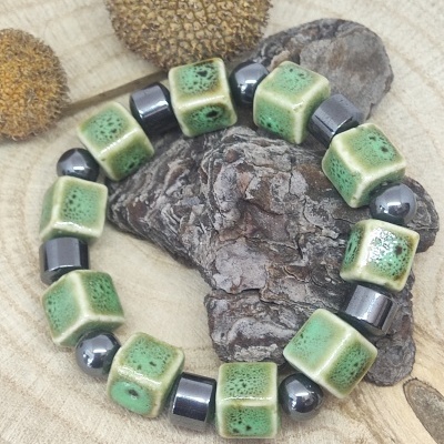 Pulseira com contas verdes de cerâmica e esferas metálicas sobre madeira clara