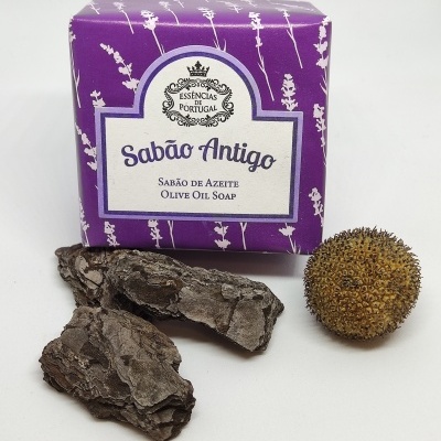 Sabão em barra embalado em roxo e branco com casca de árvore e semente ao lado