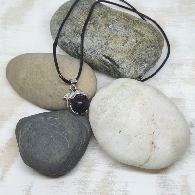 Colar com pendente em pedra preta sobre pedras lisas variadas em fundo branco.