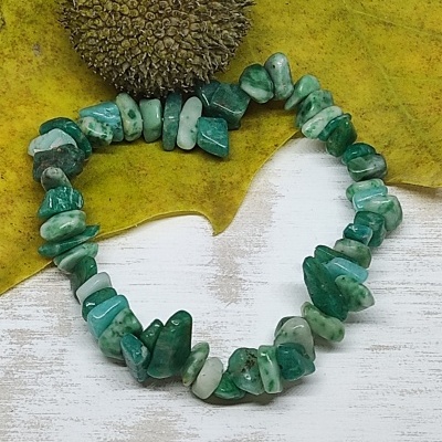 Pulseira de pedras verdes irregular sobre fundo amarelo e branco com objeto visual arredondado