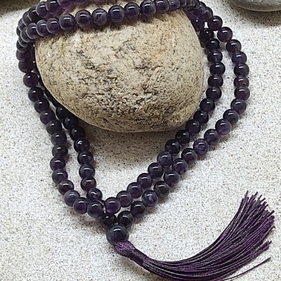 Colar de contas de ametista roxa com tassel sobre pedras e areia