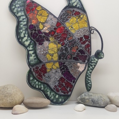 Escultura de parede borboleta em mosaico colorido com pedras e conchas ao redor
