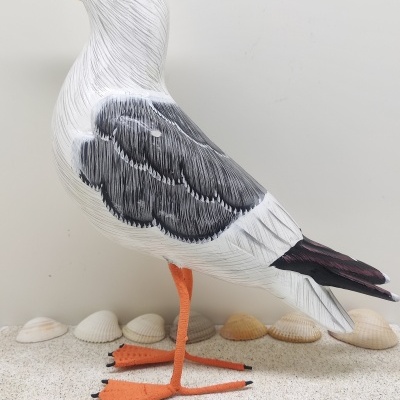 Figura decorativa de gaivota em madeira pintada sobre superfície com conchas