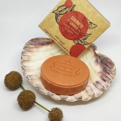 Sabonete laranja redondo numa concha com embalagem de papel e flores secas ao lado