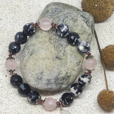 Pulseira de contas pretas, brancas e rosa com pendente prateado sobre pedra cinza