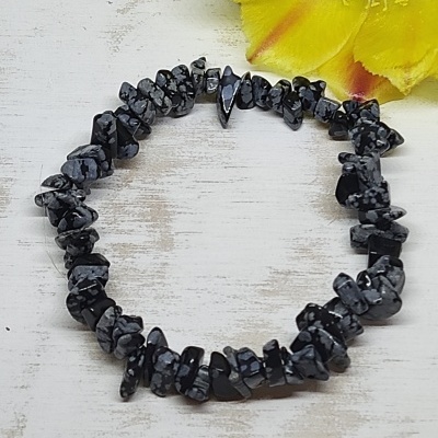 Pulseira de pedras pretas e cinzentas com padrão irregular sobre fundo de madeira clara e flores amarelas