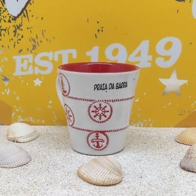 Caneca cerâmica vermelho e branco com motivos náuticos e texto Praia da Barra sobre areia com conchas e fundo amarelo com texto.