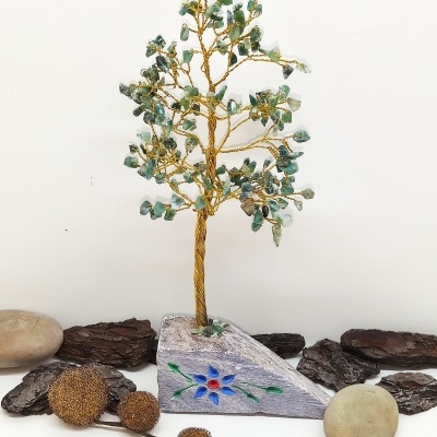 Árvore decorativa de arame dourado e pedras verdes em base com desenho floral e pedras ao redor