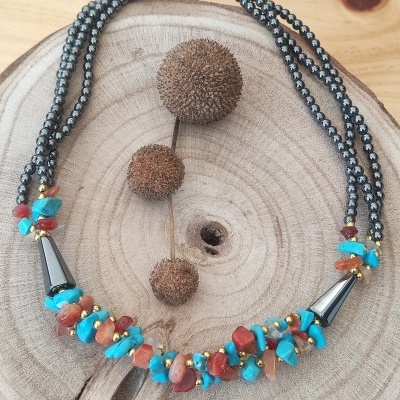 Colar com pedras turquesa e vermelhas, contas pretas e detalhes dourados sobre madeira rústica
