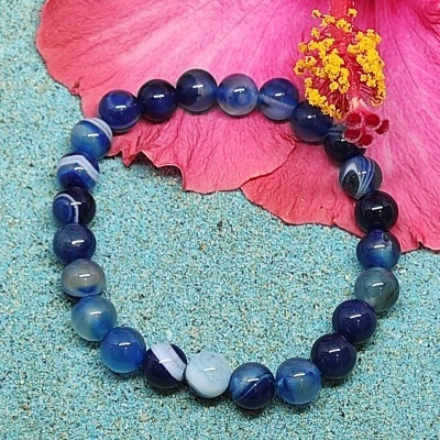 Pulseira de pedras azuis com flor rosa ao fundo sobre superfície azul