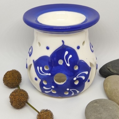 Queimador de cerâmica branco com decoração azul em forma de flor, rodeado por pedras e bolbos secos