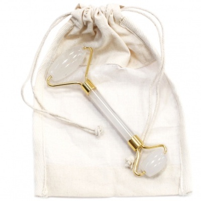 Rolo facial de pedra branca com detalhes dourados sobre saco de tecido cru