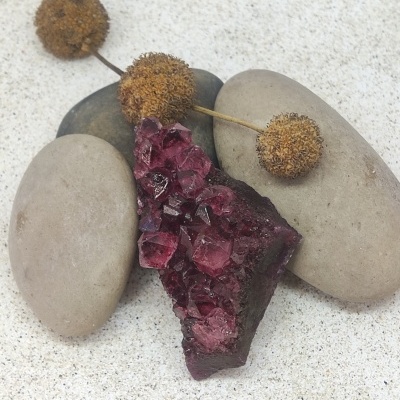 Pedra mineral com cristais roxos sobre pedras lisas e botões secos