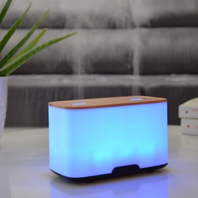 Difusor de aromas retangular iluminado em azul com tampa em madeira numa mesa branca