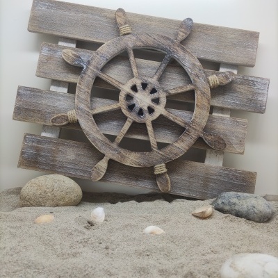 Roda de leme decorativa de madeira rústica sobre painel e areia com conchas e pedras