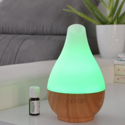 Difusor de aromas de madeira com luz verde ao lado de frasco de óleo essencial numa mesa