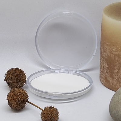 Espelho redondo aberto com tampa transparente junto a vela castanha e bagas secas