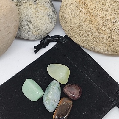 Cinco pedras polidas coloridas sobre saco de tecido preto, rodeadas por pedras maiores