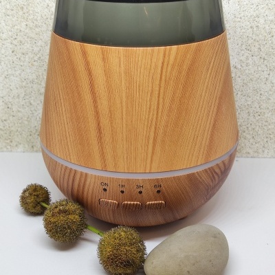 Difusor de aroma em madeira clara com cúpula translúcida escura e botões de controlo, com flores secas e pedra ao lado