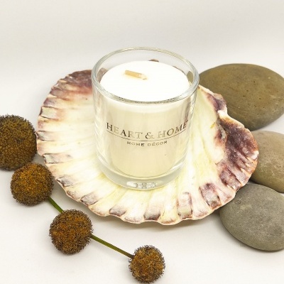 Vela em copo de vidro numa concha decorativa cercada de pedras e flores secas.