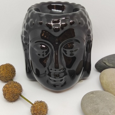 Vela de cerâmica preta em forma de cabeça de Buda com pedras e flores secas ao lado