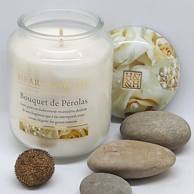 Vela em vidro branco com tampa decorativa e pedras lisas ao lado