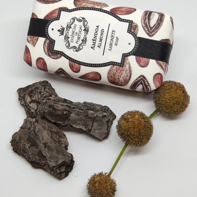 Sabonete de amêndoa embalado com padrão de amêndoas e rótulo branco e preto, casca de árvore e ramo com bolas secas castanhas