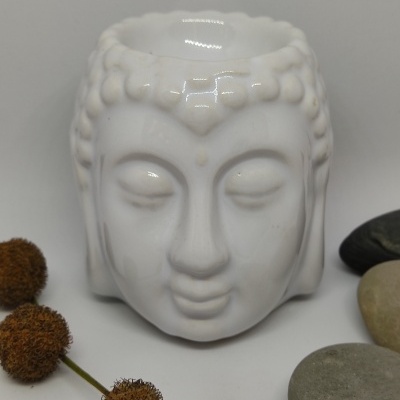 Vaso cerâmico branco em forma de cabeça de Buda com pedras e raminhos secos ao redor