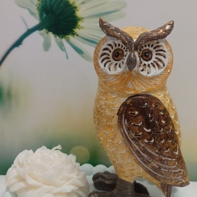 Estátua de coruja decorativa sobre base branca com flor artificial e fundo com flor margarida