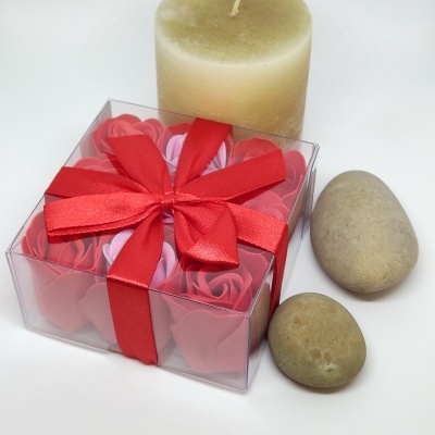 Caixa com flores de tecido vermelhas e rosas, vela creme e pedras naturais em fundo branco