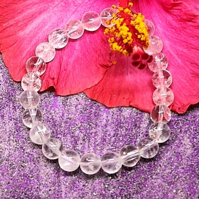 Pulseira transparente sobre superfície roxa com flor rosa