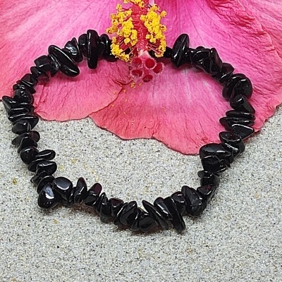 Pulseira de pedras negras irregulares com flor rosa e amarela ao fundo