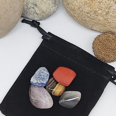 Cinco pedras polidas coloridas em saco preto de veludo rodeadas por pedras naturais maiores e ouriço do mar