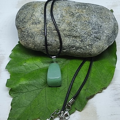 Colar com pendente verde e cordão preto sobre folha e pedra