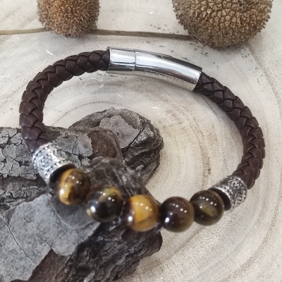 Pulseira de pele castanha com contas castanhas e amarelas e fecho metálico sobre superfície de madeira clara