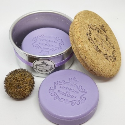 Embalagem circular em metal com tampa em cortiça e suporte roxo, texto 'ESSÊNCIAS DE PORTUGAL' e erva seca ao lado